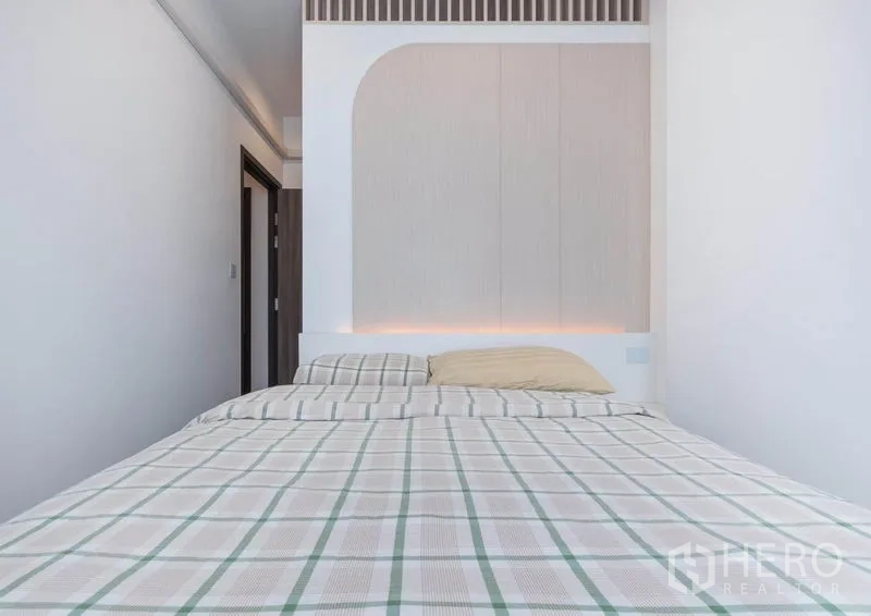 Condominium for rent in Bang Na, Bangkok - Bedroom with feature headboard, warm indirect lighting, and plaid bedding.