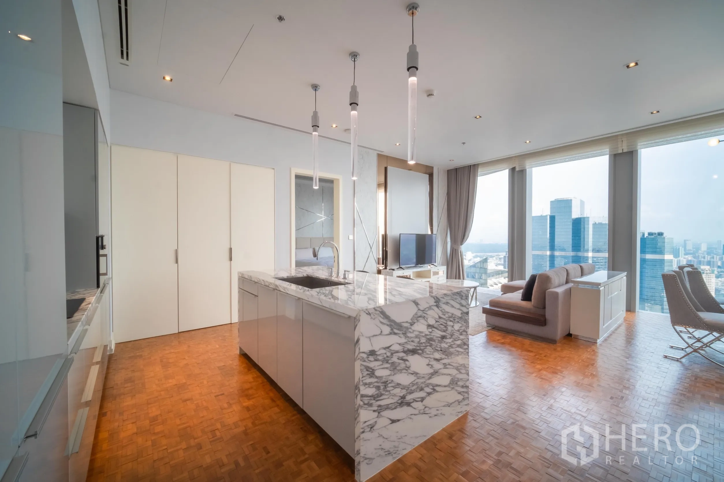 公寓 出租在Bang Rak, Bangkok - 大理石中岛厨房与客厅相连，通高落地窗与城市天际线视野。