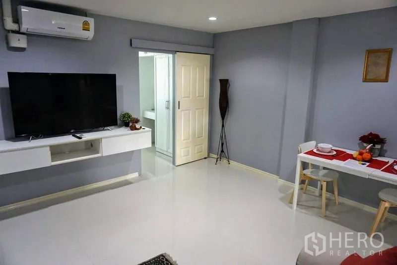 店屋 出售在Phra Khanong, Bangkok - 开放式起居区，壁挂电视、小型餐桌，门通向浴室。