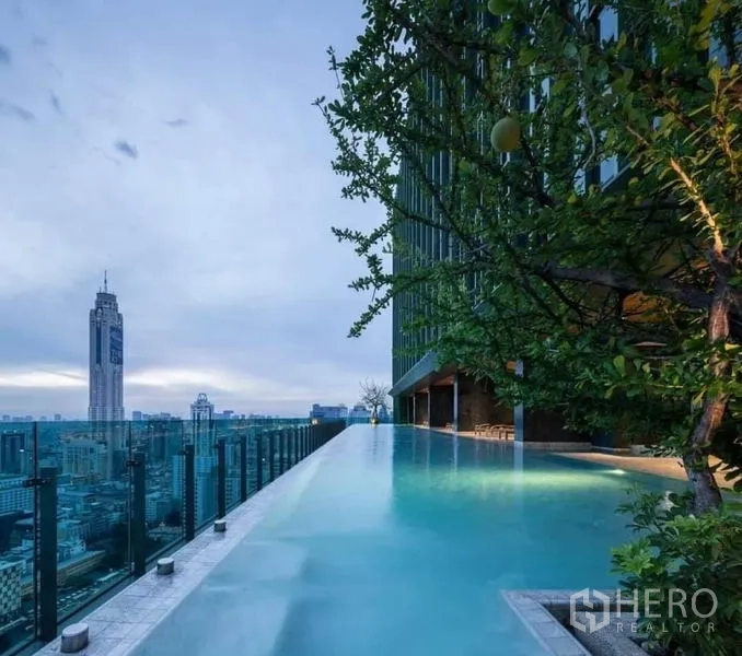 Condominium for rent or sale in Ratchathewi, Bangkok - Rooftop infinity pool with glass railing and panoramic Bangkok skyline views at dusk.