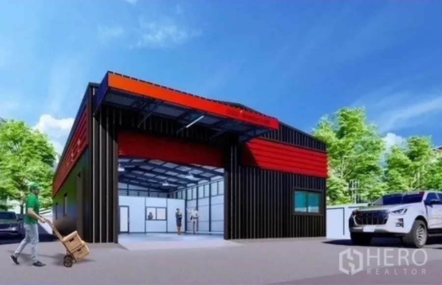 คลังสินค้า ให้เช่าหรือขายในLat Phrao, Bangkok - ภายนอกโกดังโทนสีแดง‑ดำ ประตูม้วนขนาดใหญ่ มีชายคา ทางรถเข้าและที่จอดในบรรยากาศร่มรื่น