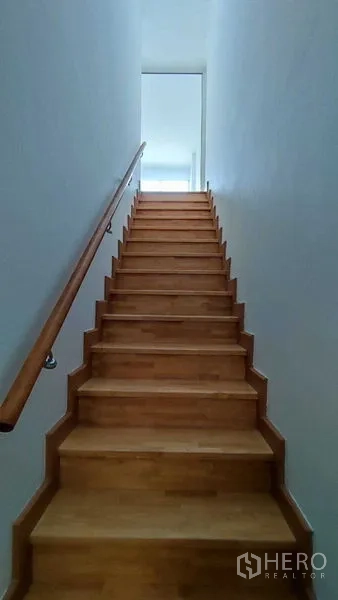 Townhouse for sale in Bang Khen, Bangkok - Wooden staircase with handrail leading to the upper floor in a bright townhouse.