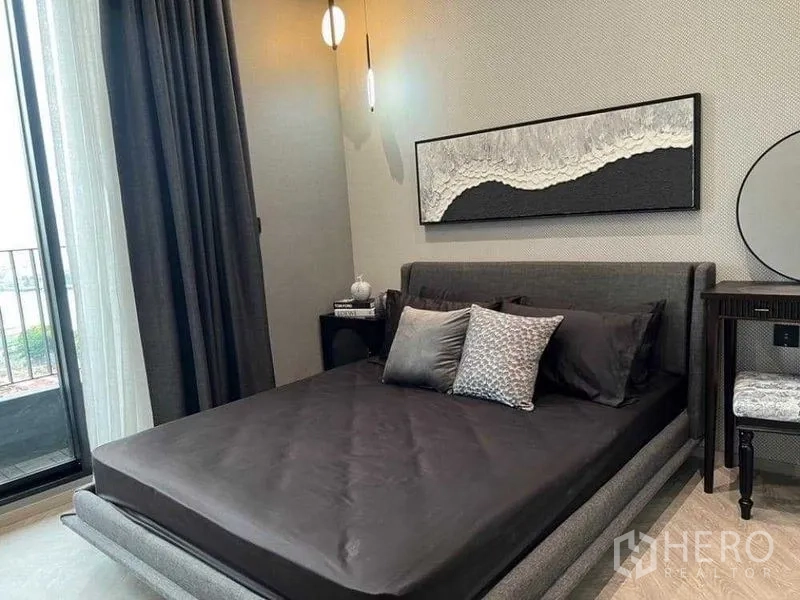 คอนโด ให้เช่าในKhlong San, Bangkok - ห้องนอนใหญ่ เตียงบุนวมโทนเข้ม เชื่อมต่อระเบียง และงานศิลป์ร่วมสมัยเหนือหัวเตียง