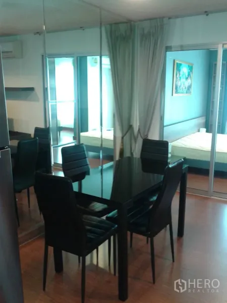 Condominium for rent in Huai Khwang, Bangkok - Dining area with glossy black table and four chairs beside a mirrored wall and sliding glass doors to the bedroom.