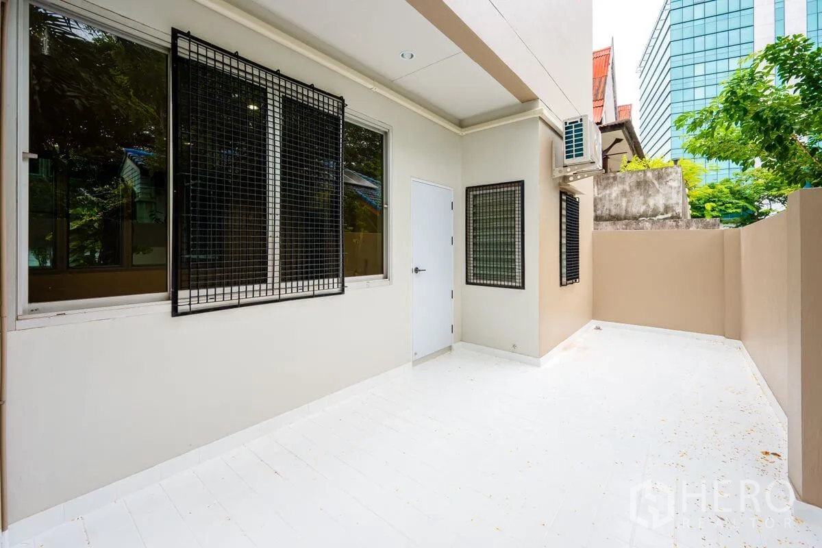 Detached House for rent or sale in Chatuchak, Bangkok - Private side patio with white flooring, metal security grilles on windows, and AC unit.