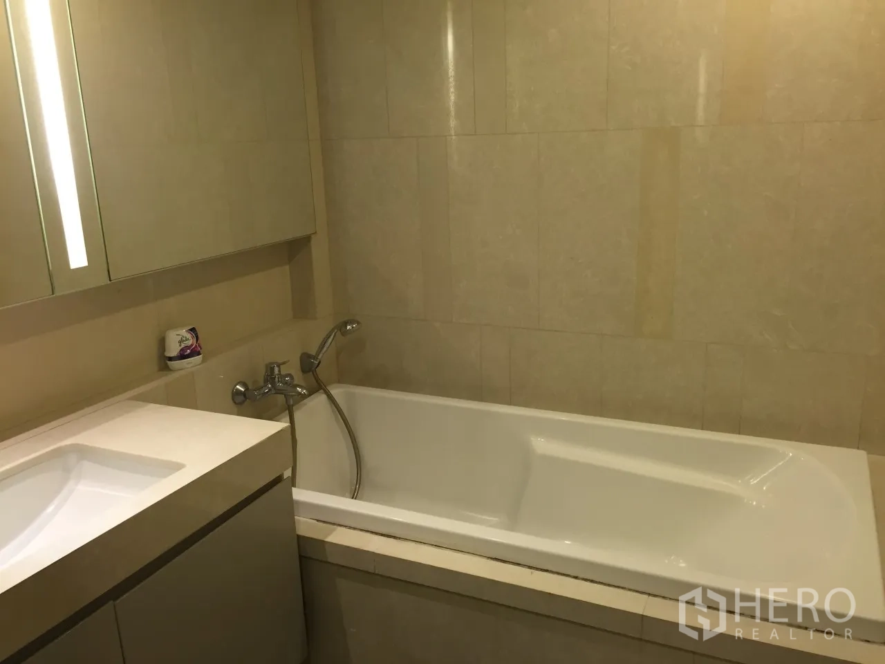Condominium for rent or sale in Watthana, Bangkok - Bathroom with vanity and soaking bathtub finished in beige tiles.
