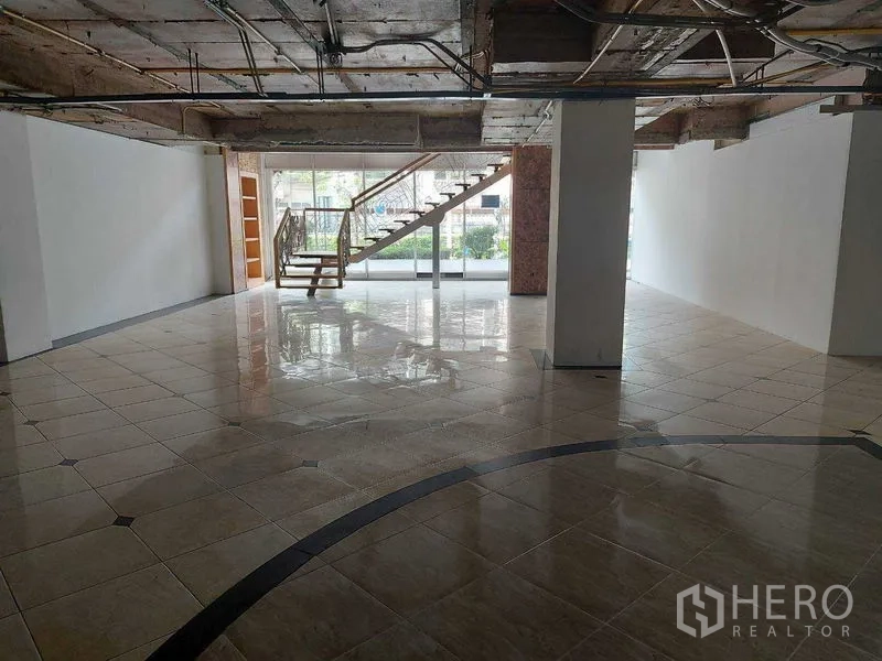 零售空间 出租在Pathum Wan, Bangkok - 一层开放式零售空间，亮面瓷砖地、整面玻璃门头与通往楼上的楼梯。