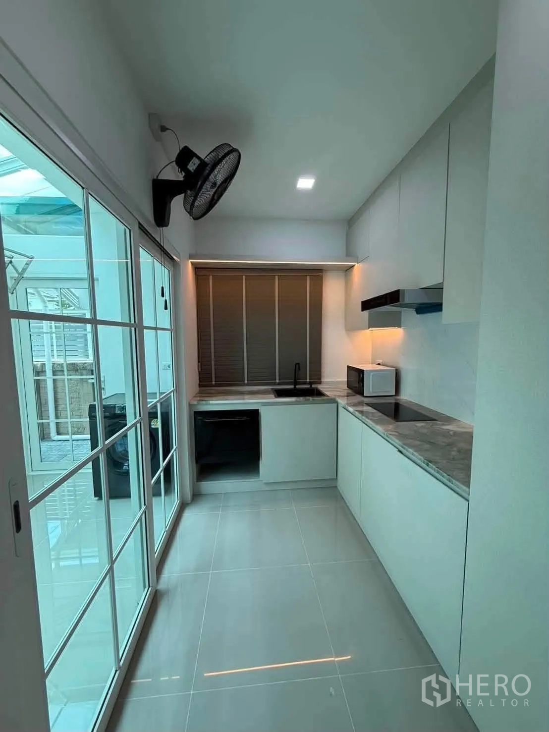 Detached House for rent in Bang Phli, Samut Prakan - Modern kitchen with sleek cabinets, cooktop, hood, sink, and sliding glass doors.