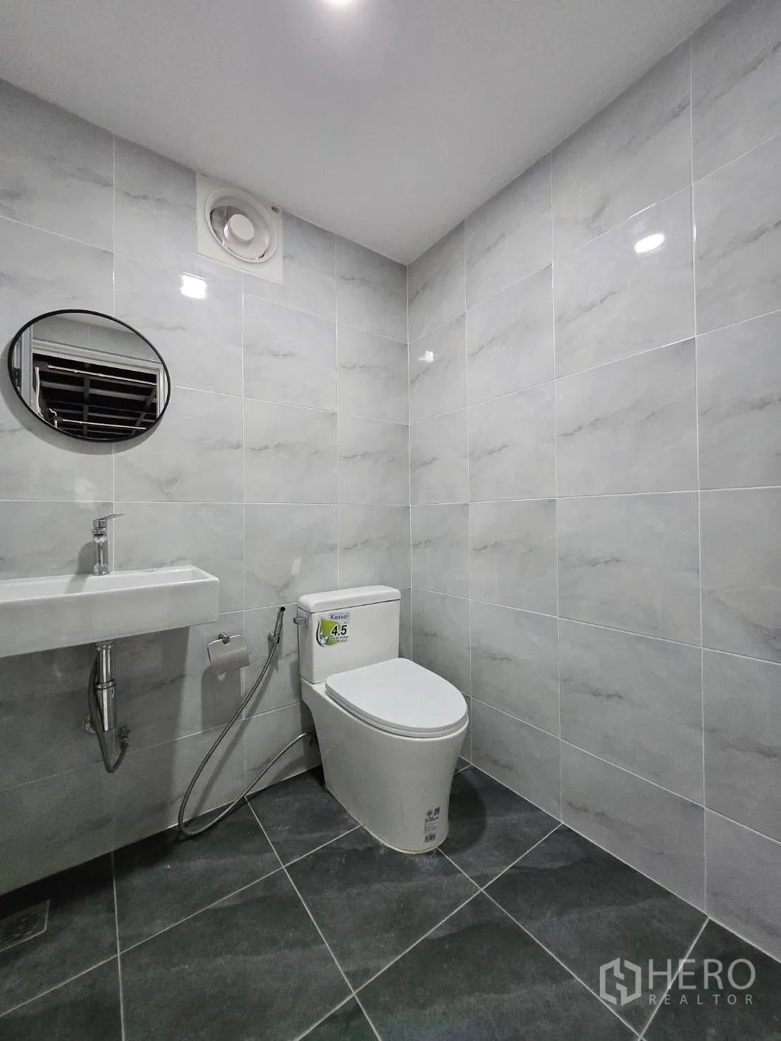 Warehouse for rent - Clean tiled restroom featuring toilet, sink, handheld bidet and ventilation fan.
