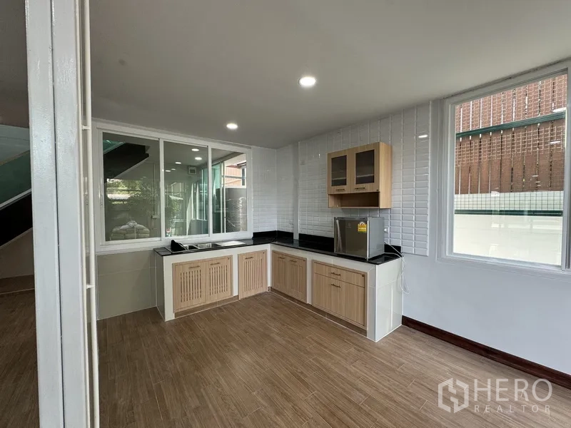 Townhouse for sale in Bueng Kum, Bangkok - L-shaped kitchen with light wood cabinets, black countertops and tiled backsplash.