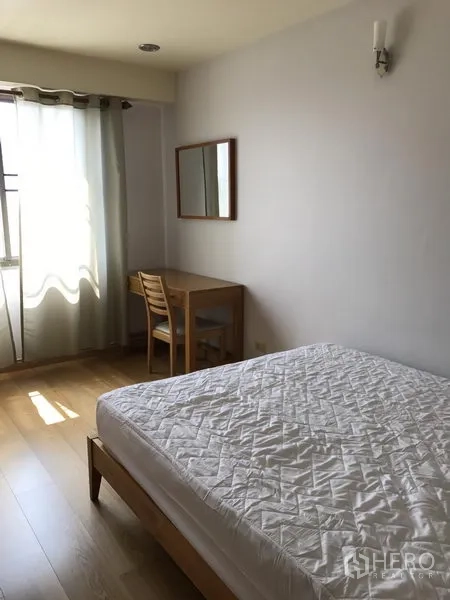 Condominium for rent in Watthana, Bangkok - Bedroom with wooden bed, study desk by the window and sheer curtains.