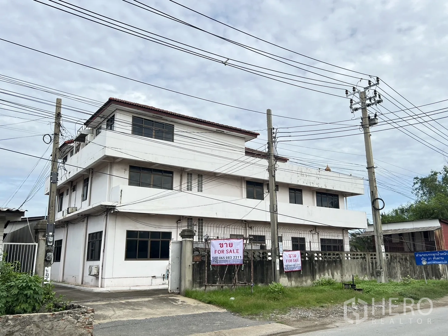 Home Office for sale in Phra Pradaeng, Samut Prakan - Oblique front view of the property set behind roadside power poles.