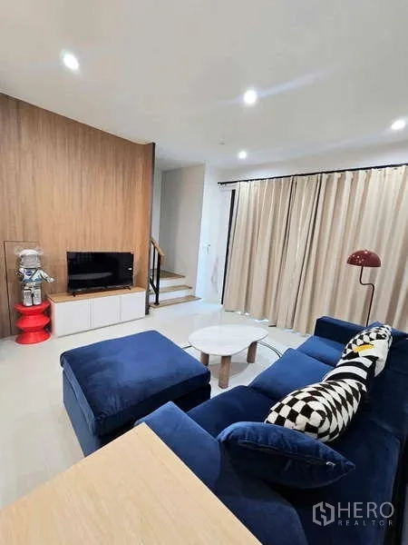 ทาวน์เฮาส์ ให้เช่าในSuan Luang, Bangkok - ห้องนั่งเล่น โซฟาสีน้ำเงิน ตู้ทีวีบิวต์อิน ผนังลายไม้ และบันได