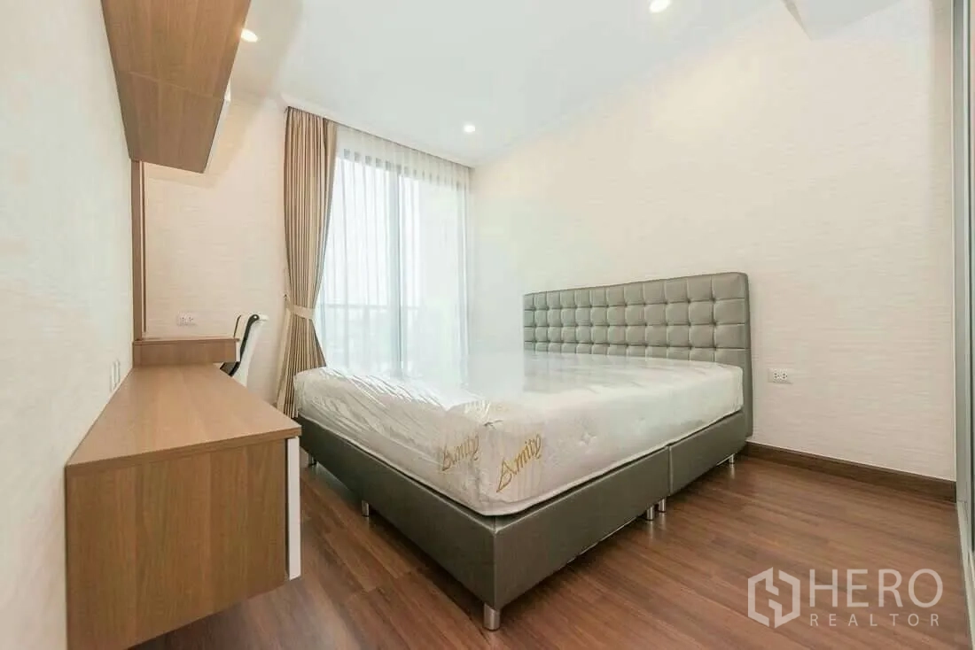 Condominium for rent in Sathon, Bangkok - Bright bedroom with tufted headboard, desk and floor‑to‑ceiling windows in a Sathon Bangkok condo.