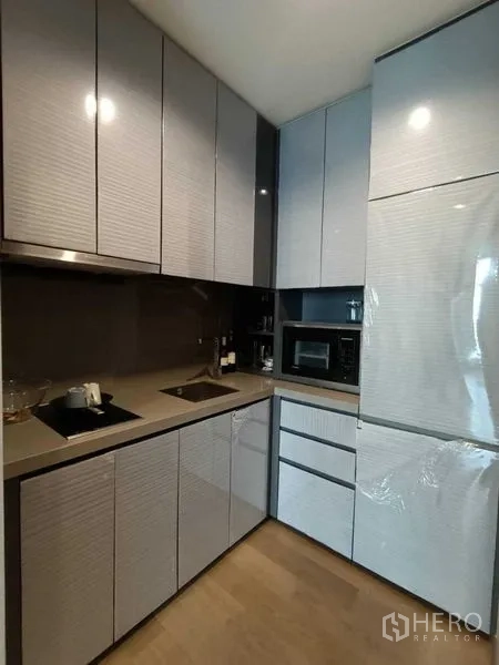 公寓 出租或出售在Bang Rak, Bangkok - L型独立厨房，配备时尚柜体、灶台、水槽、微波炉与大冰箱。