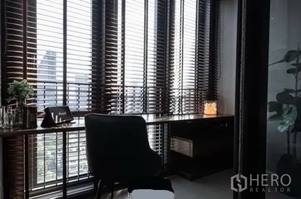 公寓 出租在Khlong Toei, Bangkok - 角落书房，长书桌贴近落地窗，百叶帘外是城市景观。