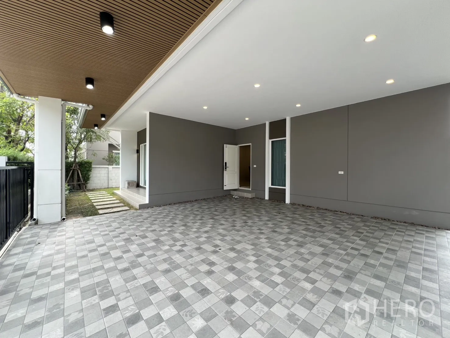 Detached House for rent in Lat Krabang, Bangkok - Covered carport with tiled floor, wood slat ceiling lights, and side entry steps beside a small lawn.