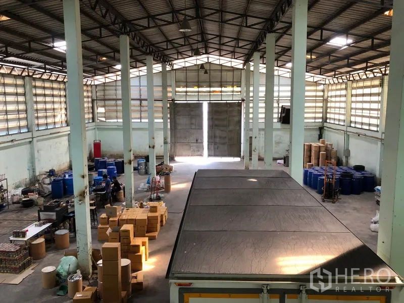 货栈 出租在Nonthaburi - 从夹层俯瞰仓库，双开金属装卸门，立柱与货品区。