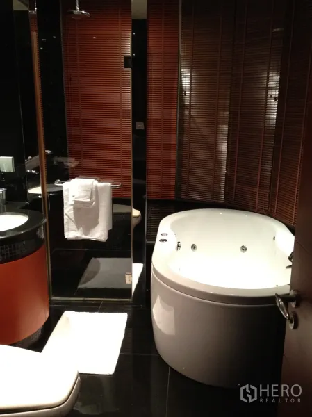 Condominium for rent in Bang Rak, Bangkok - Modern bathroom featuring a round jacuzzi bathtub, glass shower enclosure and glossy black floor tiles.