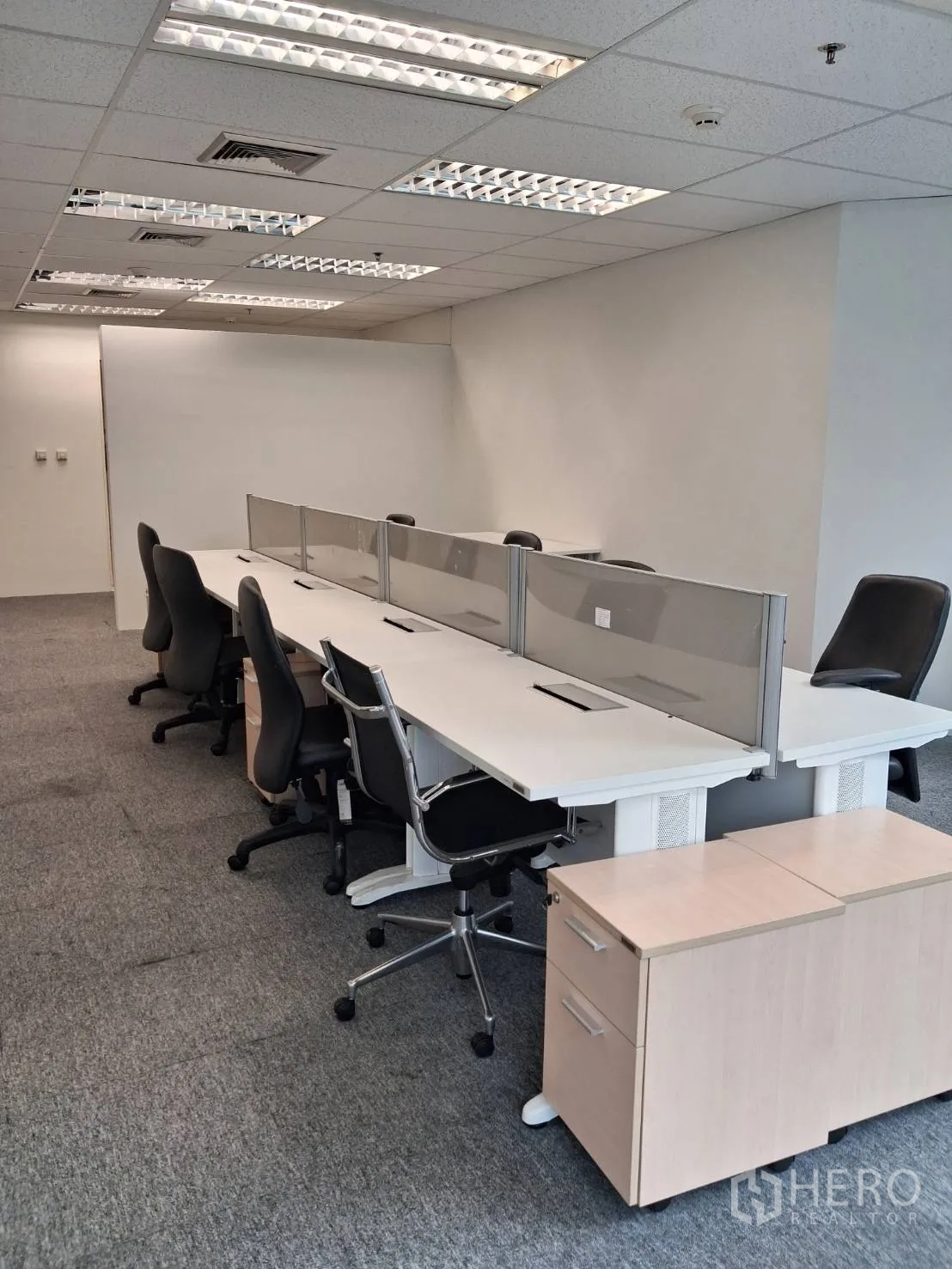 Office Space for rent in Sathon, Bangkok - Row of workstations with divider screens under grid ceiling lights on grey carpet.