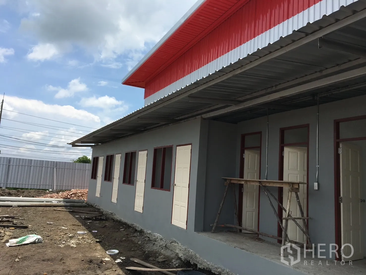 仓库 for sale in Sai Noi, Nonthaburi - 建筑侧立面，多扇门位于带顶走道下，现场可见管线施工。