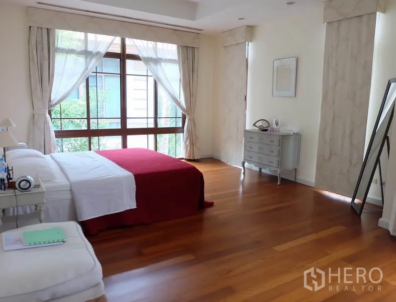 Detached House for rent in Watthana, Bangkok - Airy master bedroom with wood floors, large windows, sheer curtains, and a red bed throw.