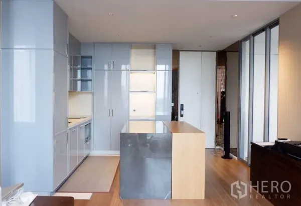 Condominium for sale in Khlong Toei, Bangkok - Open-plan kitchen featuring glossy built-in cabinets, a stone-topped island, and wood flooring.
