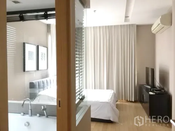 คอนโด ให้เช่าในKhlong Toei, Bangkok - ห้องนอนหลักพร้อมผนังกระจกกั้นห้องน้ำมีอ่างอาบน้ำ เตียง ทีวีคอนโซล และเครื่องปรับอากาศติดผนัง