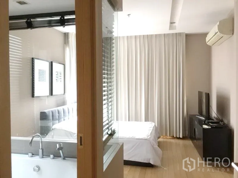 คอนโด ให้เช่าในKhlong Toei, Bangkok - ห้องนอนหลักพร้อมผนังกระจกกั้นห้องน้ำมีอ่างอาบน้ำ เตียง ทีวีคอนโซล และเครื่องปรับอากาศติดผนัง