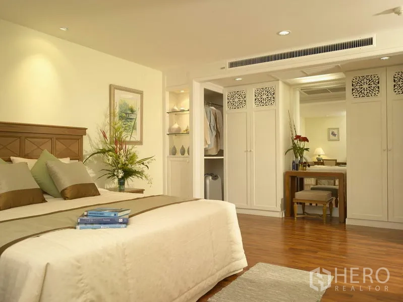 Apartment for rent in Bang Rak, Bangkok - Master bedroom angle with built-in wardrobes, dressing table and walk-in closet on wood flooring.