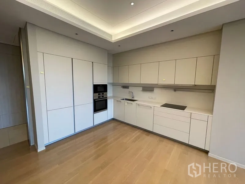 Condominium for rent or sale in Pathum Wan, Bangkok - Sleek L-shaped kitchen with ample cabinets, built-in oven and induction cooktop.