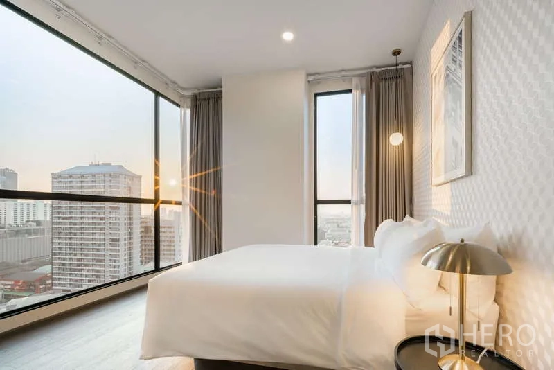 Condominium for rent - Corner bedroom with floor-to-ceiling windows offering panoramic Bangkok skyline at sunset.
