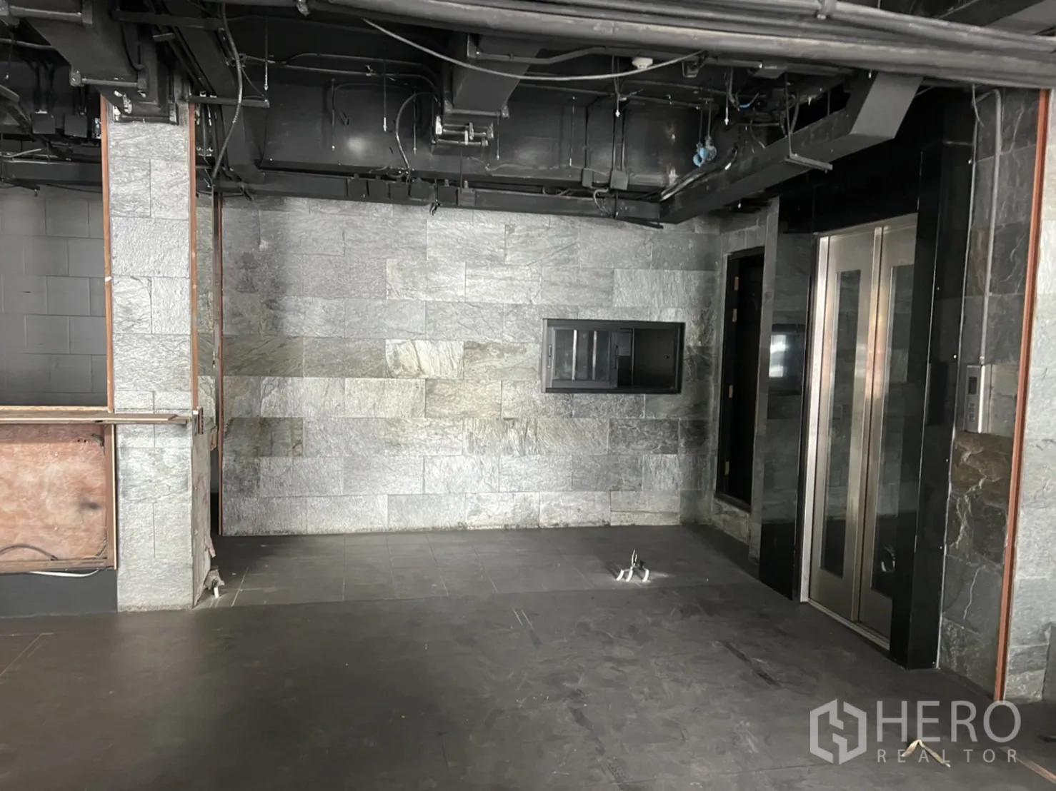 零售空间 出租在Khlong Toei, Bangkok - 灰色石材墙面的大厅，配乘客电梯、外露管线与设备点位。