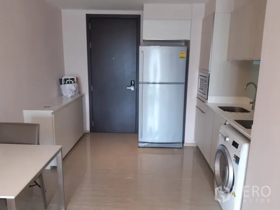 Condominium for rent or sale in Watthana, Bangkok - Entryway view of the open-plan kitchen with full-size fridge and a dining table.