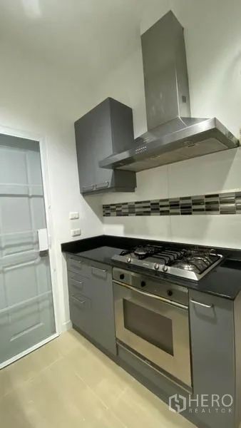 Townhouse for rent in Wang Thonglang, Bangkok - Compact modern kitchen with gas stove, oven, range hood, and tiled backsplash.