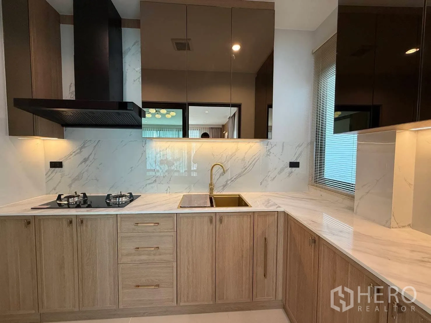 Detached House for rent in Bang Phli, Samut Prakan - Modern L-shaped kitchen with marble-look backsplash, gas hob, gold sink faucet, and wood cabinets.