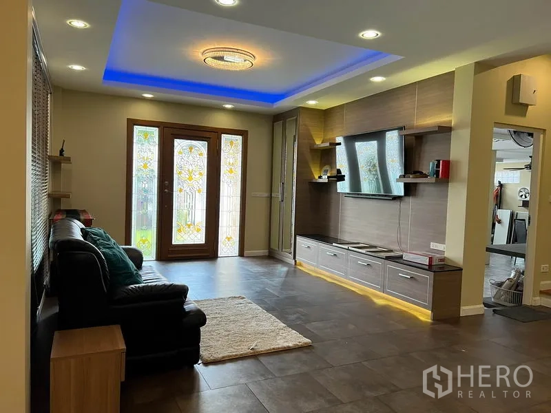 Detached House for rent in Bang Kapi, Bangkok - Modern living room with cove lighting, built-in TV wall and stained-glass double doors.