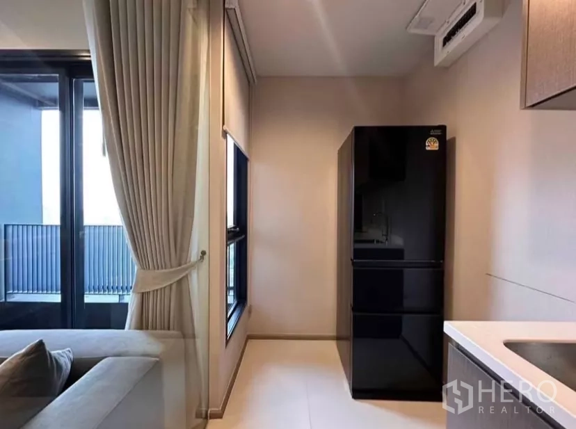 Condominium for rent in Chatuchak, Bangkok - Kitchen corner with tall black refrigerator next to window and balcony door.