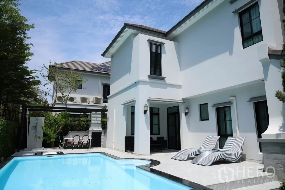 Detached House for rent or sale in Saphan Sung, Bangkok - Rear exterior with private swimming pool, striped sun loungers, patio seating, and lush garden.