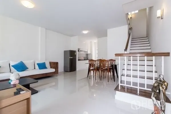 Townhouse for rent in Watthana, Bangkok - Open-plan living and dining area with staircase, white walls, glossy tile floors and kitchenette in a Watthana townhouse.