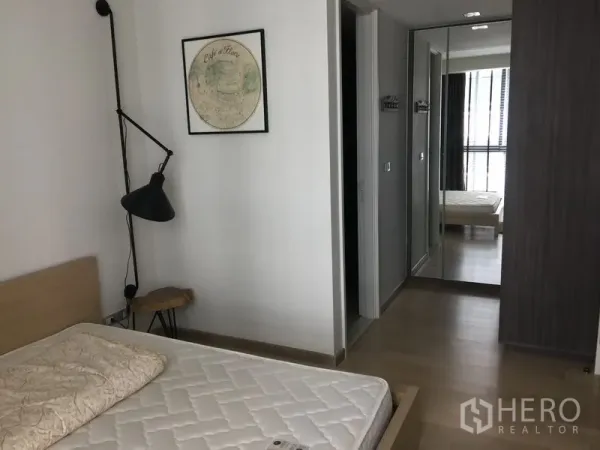 公寓 出租在Watthana, Bangkok - 卧室角度展示镜面衣柜、床头灯与通往浴室的门。