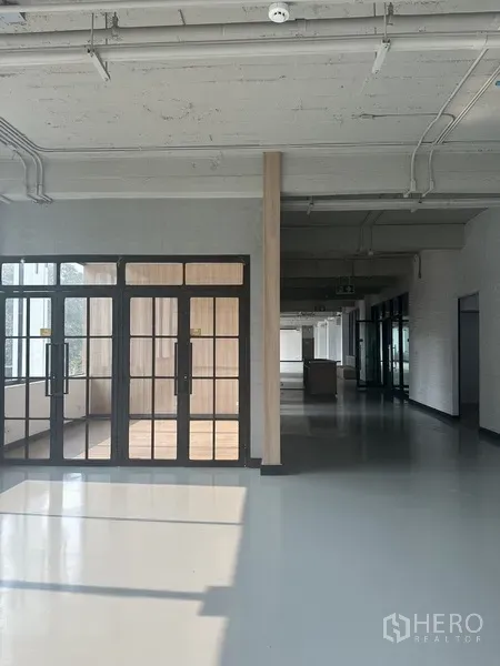 Office Space for rent - Entrance with black-framed glass doors opening to a bright corridor in the office.