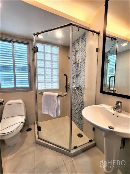 公寓 出租在Bang Rak, Bangkok - 紧凑浴室，玻璃淋浴房、马桶、柱式洗手台与马赛克装饰墙。