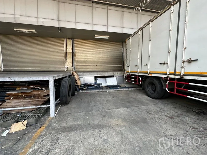 Warehouse for rent in Lam Luk Ka, Pathum Thani - Close-up of a raised loading dock with roller shutters beside a large delivery truck.