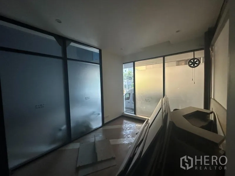 Office Space for rent in Khlong Toei, Bangkok - Compact front room with floor-to-ceiling frosted windows and stacked renovation materials.