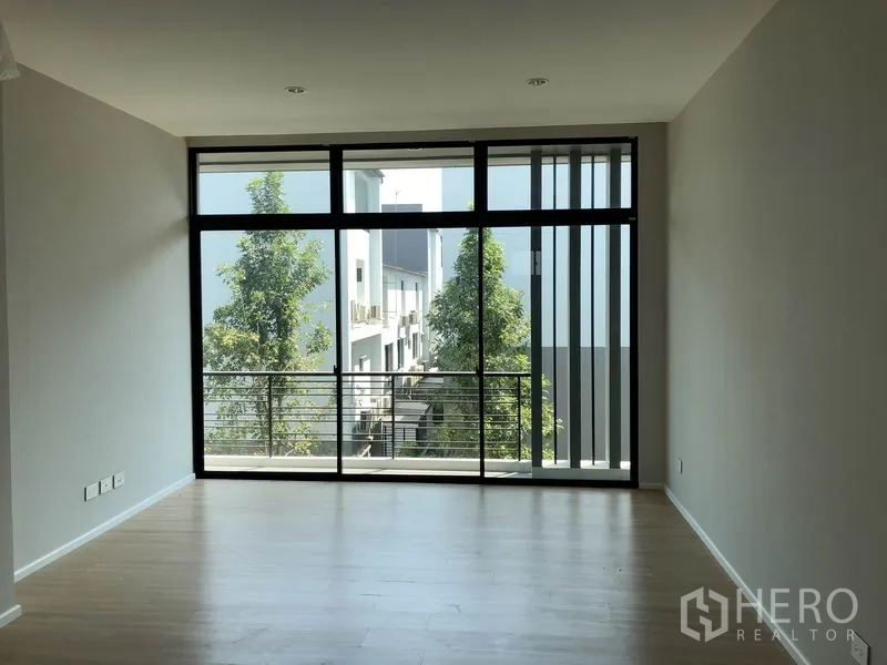Townhouse for sale in Saphan Sung, Bangkok - Open-plan room with full-height windows and a balcony railing bringing in natural light.
