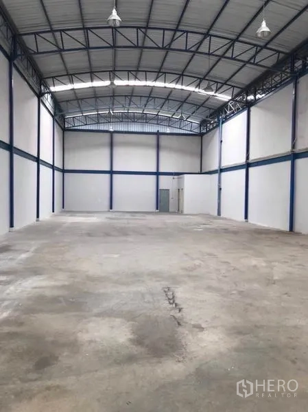 Factory for rent or sale in Mueang Samut Sakhon, Samut Sakhon - High-ceiling warehouse hall with steel truss roof, concrete floor and service door.