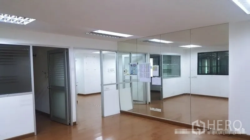 Warehouse for rent in Suan Luang, Bangkok - Glass-partitioned office inside the warehouse with mirrored wall and fluorescent lighting.