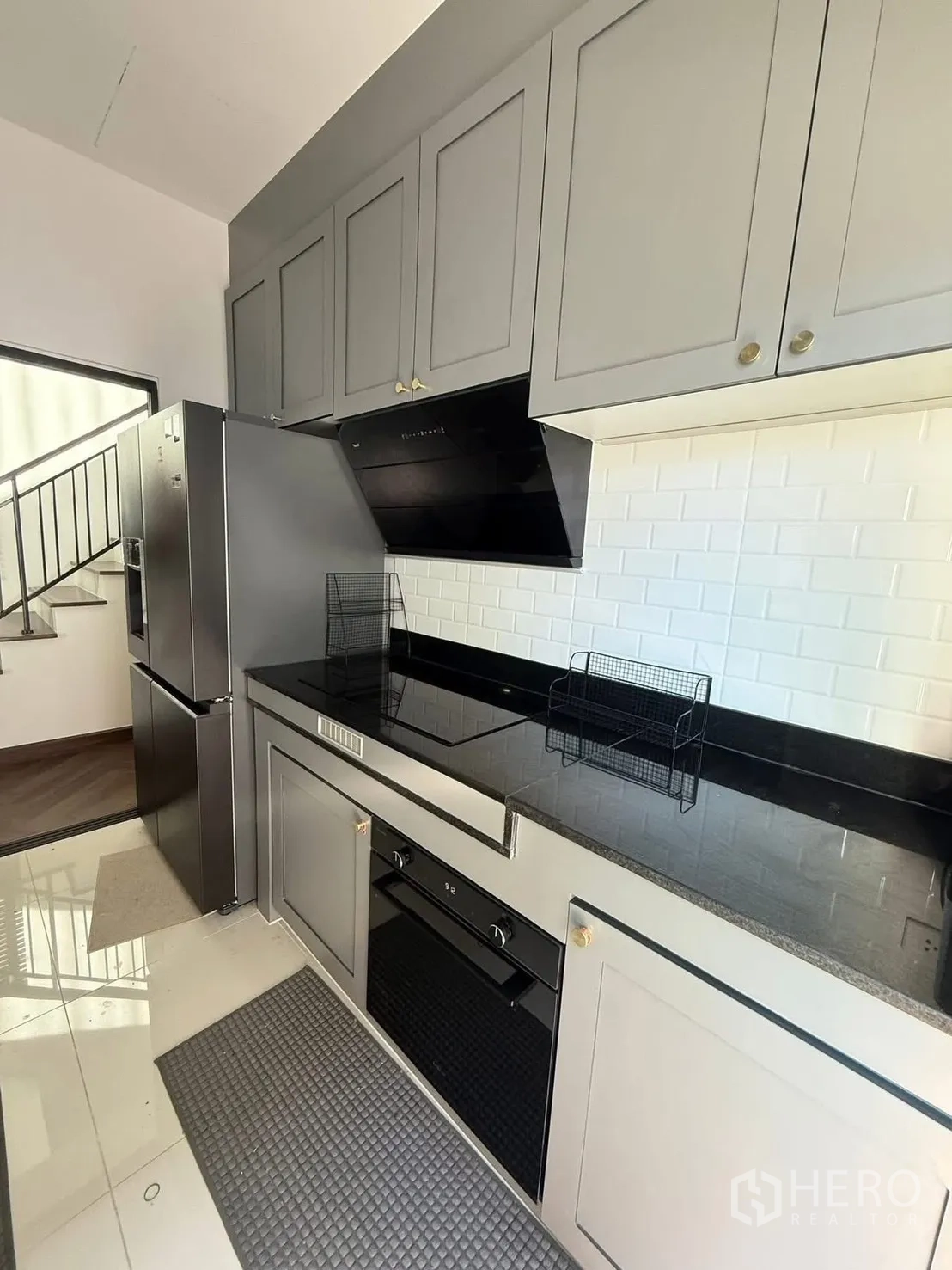 Detached House for rent in Bang Phli, Samut Prakan - Closed kitchen with black countertops, hob, hood and oven beside the fridge.