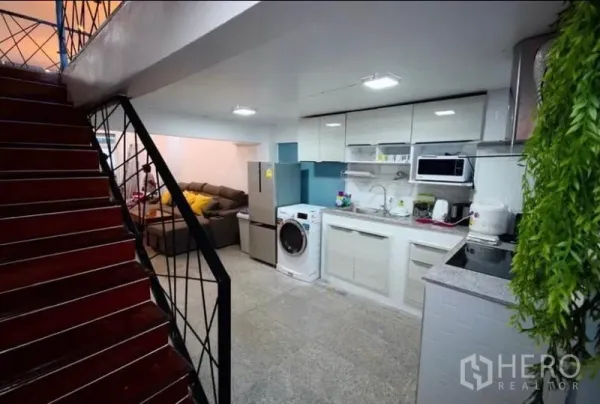 Townhouse for rent in Ratchathewi, Bangkok - Open kitchen with white cabinets and appliances beside a staircase.